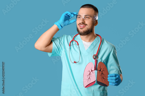 Male doctor in AR glasses with paper lungs on blue background