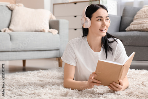 Young woman in headphones listening to audiobook on carpet at home