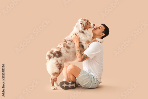 Young man with Australian Shepherd dog hugging on beige background