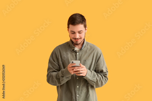 Handsome young man using mobile phone on yellow background. Online dating con...