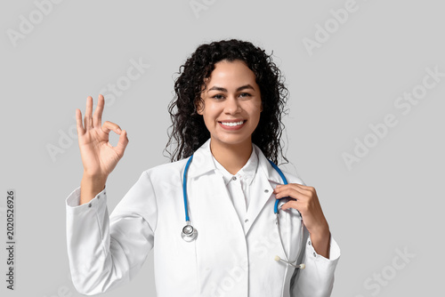 Beautiful young happy African-American female doctor with stethoscope showing...
