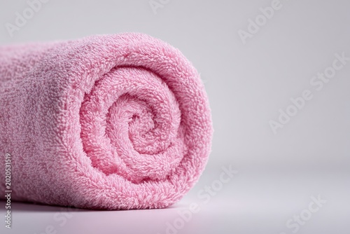 Rolled-up pink towel with a spiral center sits on a plain, light gray surface