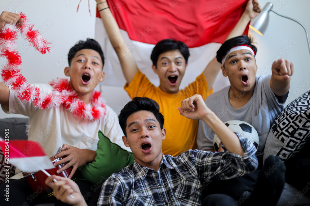 Obraz premium Group of passionate Indonesian Football Fans Shouting and Cheering with National Flag and Ball