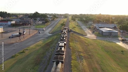 Aerial Drone View of Moving Train on Train Tracks Moving Along Roads Near Industrial Train Yard Surrounded By Grass and Buildings in Rural Town of Sweetwater, Texas