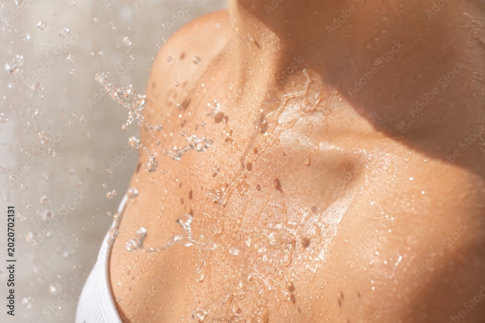 Fototapeta premium Close up of sunlit wet shoulder and neck with splashing water droplets, glowing skin texture, refreshing summer skincare and wellness concept