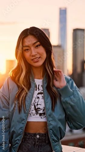 Stylish Young Woman in Bomber Jacket Posing on City Rooftop at Sunset. Vertical video