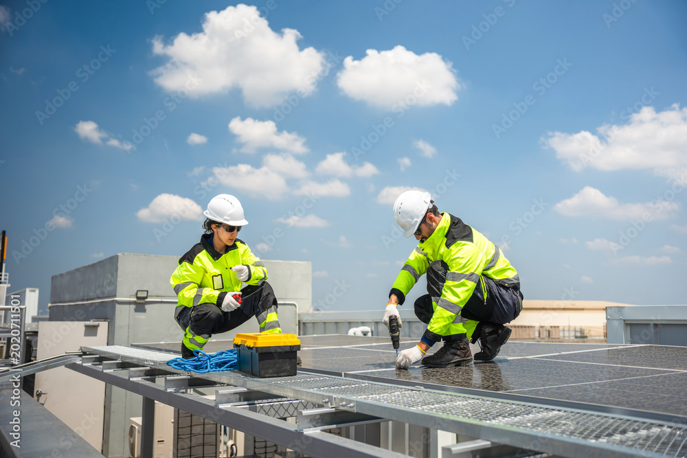 Fototapeta premium Engineers installing solar panels on rooftop with electric drill, Technicians in reflective jackets maintaining solar energy system, Team of workers installing photovoltaic panels on building roof