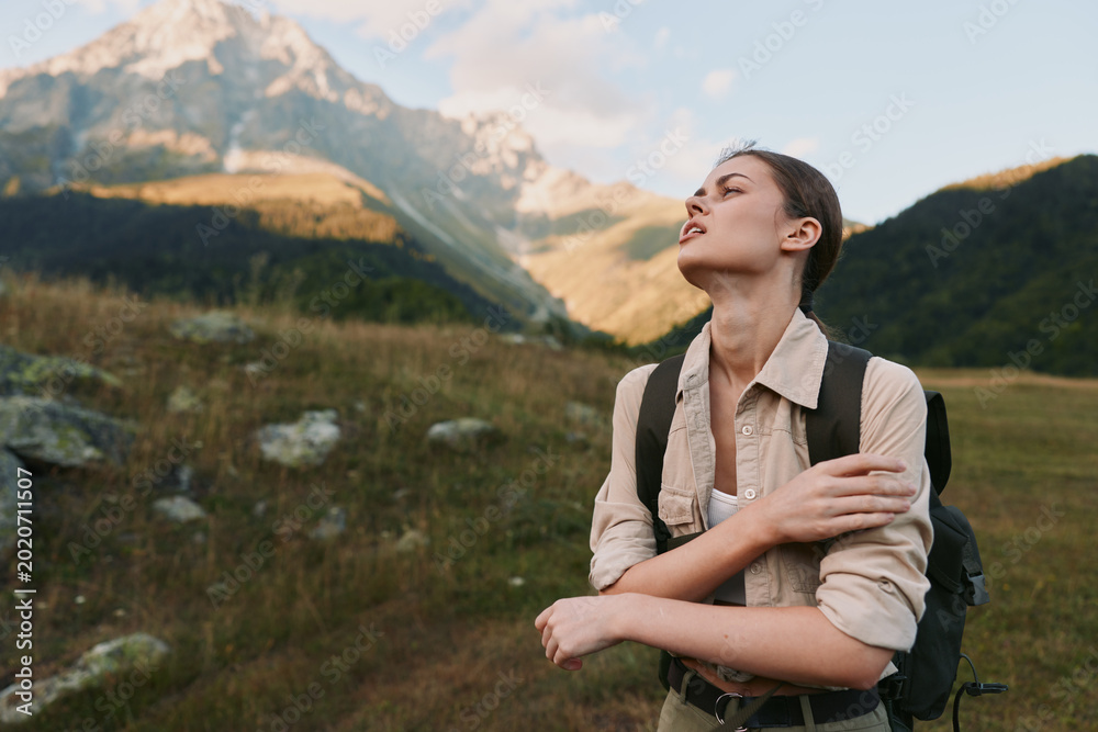 Obraz premium A woman outdoors with a backpack stands among mountains, eyes closed, face lifted to the sun, embodying freedom, resilience, and personal discovery.