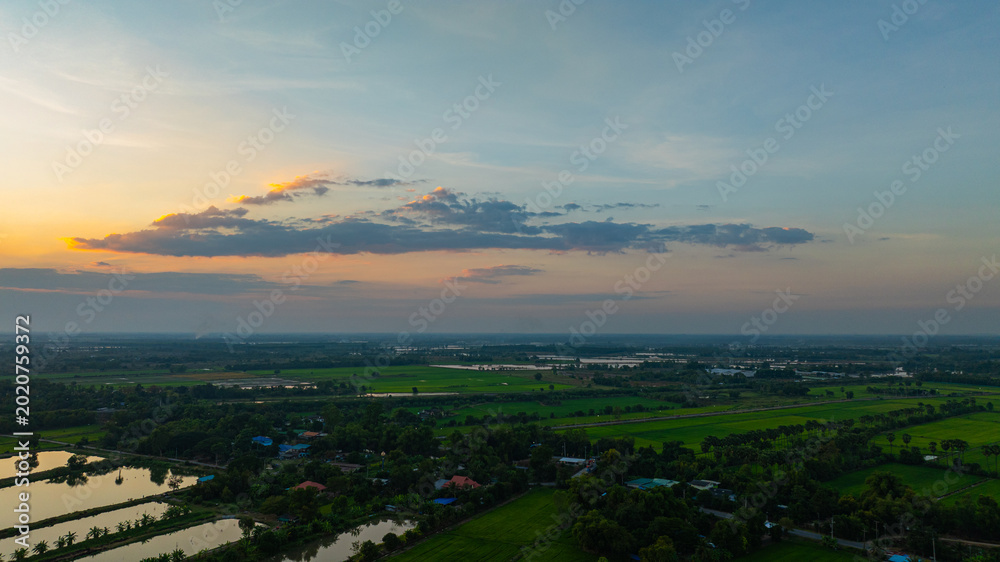 Obraz premium A stunning golden sunset reflecting on a calm lake surrounded by rural greenery and tree silhouettes. The dramatic clouds and warm evening light create a peaceful natural landscape perfect for travel