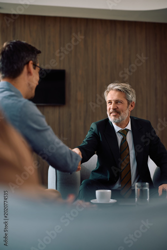 Happy financial advisor handshaking with client after successful meeting in office.