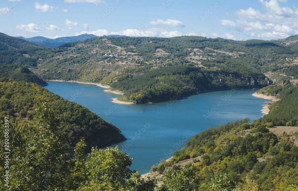 Fototapeta premium Stunning sunset over a calm river bordered by lush forests and rolling hills. Warm evening light reflects on the tranquil water, creating a peaceful natural landscape ideal for themes of wilderness