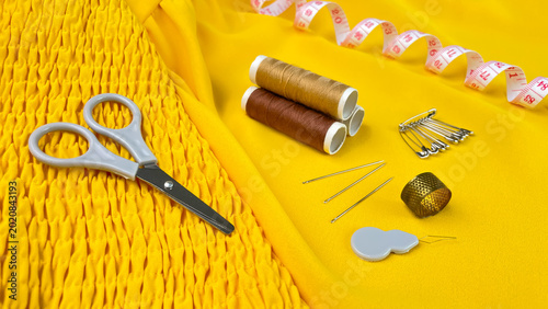 Foto A close-up of scissors, thread, needles, pins, and a thimble on bright yellow fabric