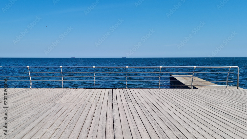 Αυτοκόλλητο Wooden boardwalk with metal railing overlooking sea horizon and pier