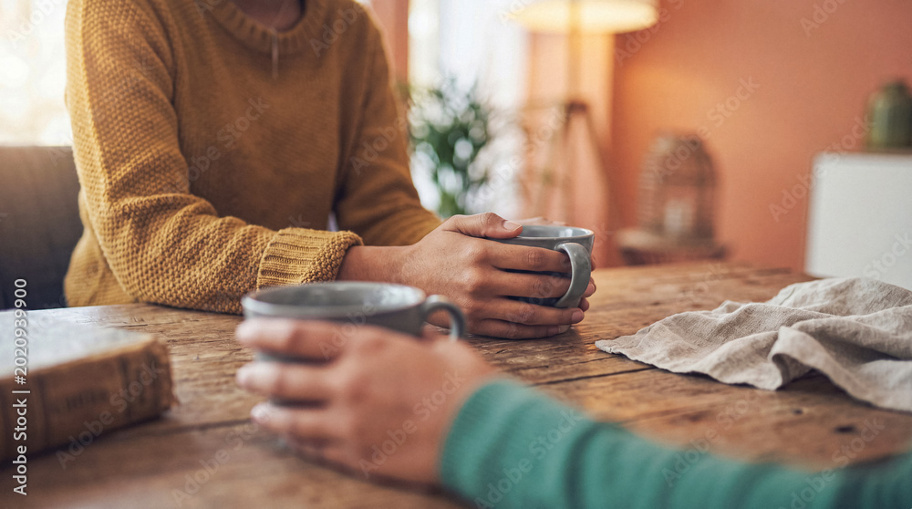 Αυτοκόλλητο Two pairs of hands holding warm coffee mugs on a rustic wooden table, symbolizing connection and shared moments