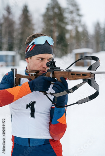 Biathlon athlete aims down sights with rifle during snowy competition.