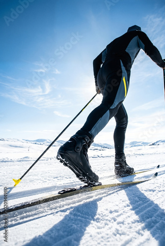 Athlete strides across a snowy landscape during cross-country skiing competition.