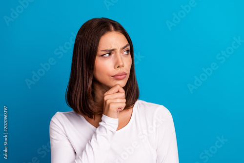 Obraz na plátne Thoughtful young woman with a brown bob wearing a white shirt stands against a b