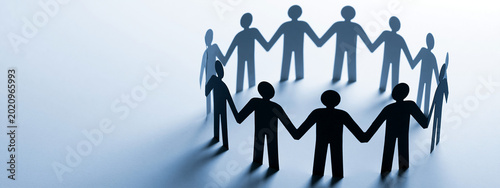 Conceptual image of paper cutout human figures holding hands in a circle representing teamwork, global unity, community support, and strong partnership on a clean blue background with copy space.