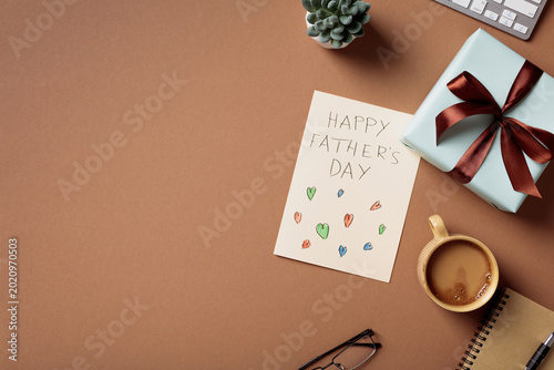 Happy Father's Day greeting card with gift box and coffee on brown office desk flat lay