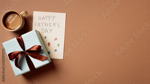 Minimalist Father's Day composition with gift box, card and coffee on brown background