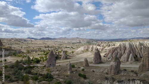 A wide-angle panoramic view showing the vastness of the Cappadocia valley with scattered fairy chimney rock formations and distant mountains.