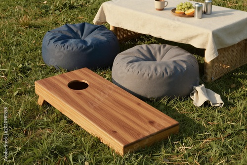 Wooden cornhole board beside low table and cushion seating outdoors