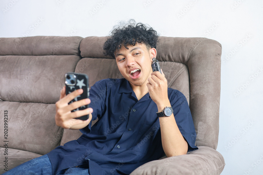 Fototapeta premium Young Asian Man Taking Selfie Holding Vape Device On Sofa