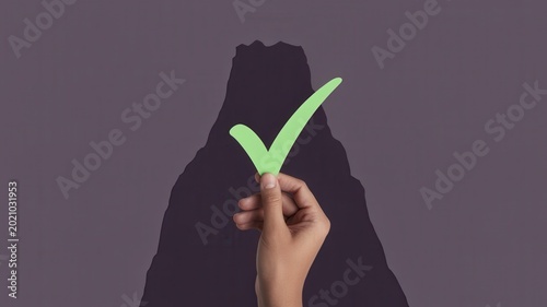 A hand holds a green checkmark in front of a dark mountain.
