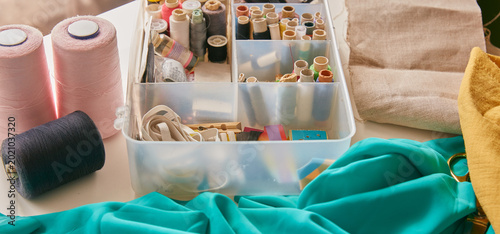 Tableau sur toile Sewing kit with colorful thread spools and fabrics on a work table