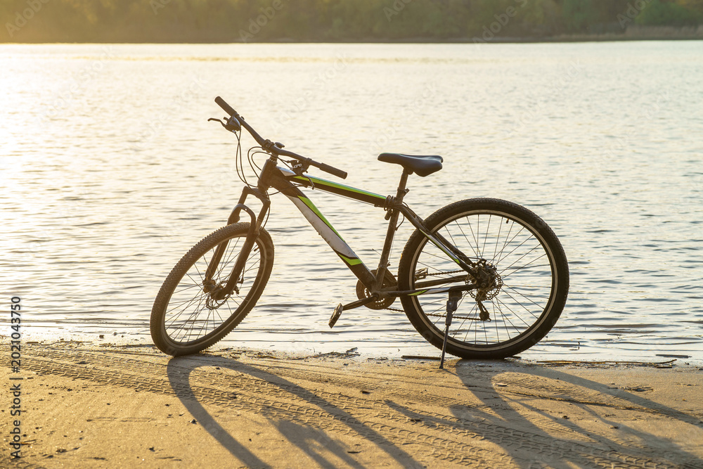 Fototapeta premium A bicycle parked on the riverbank, with sunlight reflecting off the water surface.