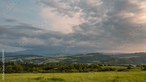 Cinematic 4K timelapse of the Tatra Mountains and Czorsztyn Lake at sunset. Panoramic view featuring Niedzica Castle, vibrant green summer meadows, and dynamic storm clouds over rural Poland.