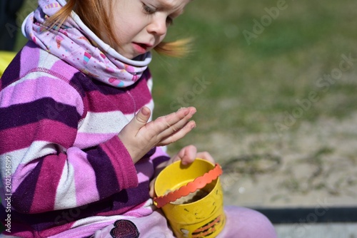 Toddler girl examining sand on her hands while playing in a sunny playground sandbox, enjoying sensory outdoor activities and creative childhood exploration.