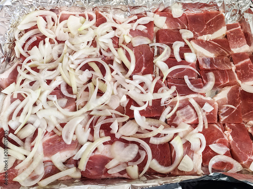 Foto Sliced raw pork topped with sliced onions on foil tray for cooking preparation a
