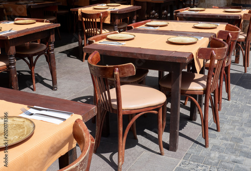 Outdoor restaurant terrace with wooden tables and chairs prepared for guests in sunny weather