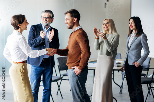 Group of diverse business professionals in an office setting, a man and woman making a handshake while colleagues are happily clapping