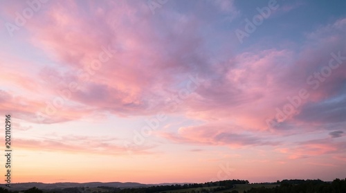 Serene sunset landscape with pink clouds over rolling hills and trees.AI generated