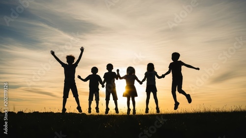 Silhouetted children jumping happily at sunset, holding hands