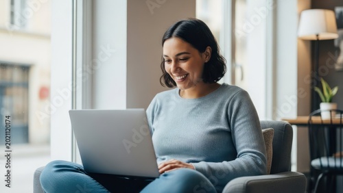 Smiling woman using a laptop seated in a chair near a window