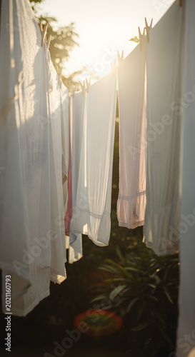 White bedsheets drying on clothesline outdoors in warm golden hour sunlight.