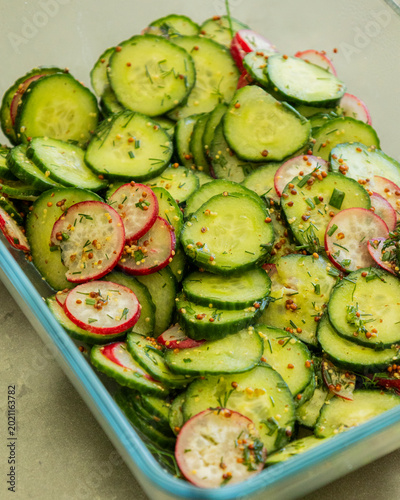 spring salad with cucumber radishes and honey mustard dressing in a bowl close up