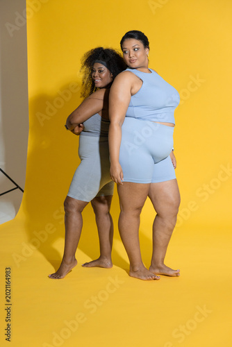 Valokuva Diverse female models posing back-to-back in studio on yellow backdrop, wearing