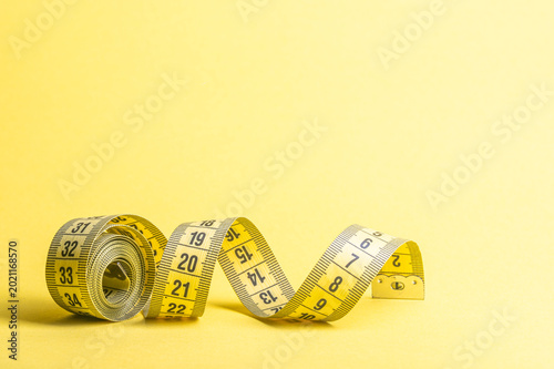 Measuring tape on yellow background displays numbers for diet and fitness tracking
