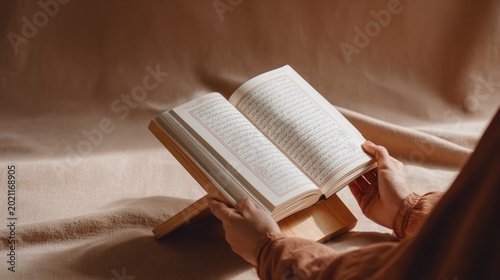 Hands holding open quran on wooden stand amidst soft light and warm tones