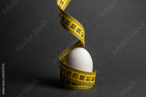 A white egg on a dark surface, wrapped in yellow tape, highlights nutrition and diet