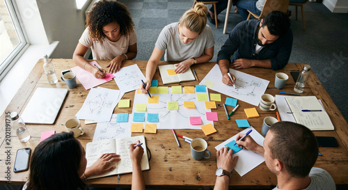 Top view of a creative diverse team brainstorming ideas with sticky notes on a wooden table.