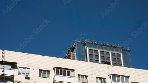 Modern glass skyscraper under construction with a yellow tower crane on top against a clear blue sky. Low angle view of contemporary urban development and high-rise architecture in Kyiv, Ukraine.