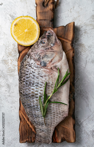 Fresh raw tilapia fish on a rustic wooden board with lemon and rosemary.