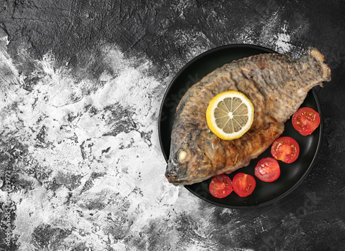 Roasted tilapia fish served with lemon slice and cherry tomatoes on a black plate.