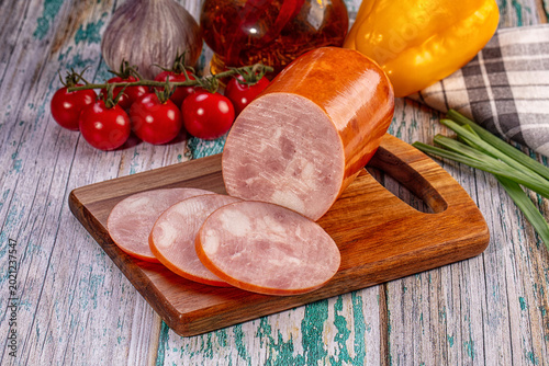 Obraz na płótnie Sliced ham sausage on wooden cutting board with fresh cherry tomatoes and garlic