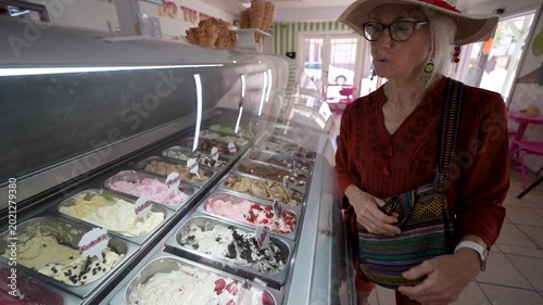 Mature woman stands by an ice cream counter in Santa Rosalia. She enjoys the options available and looks excited to choose her treat.